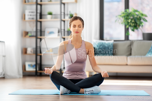 Image of woman doing yoga in lotus pose at home