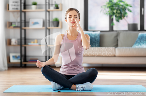 Image of woman doing yoga in lotus pose at home