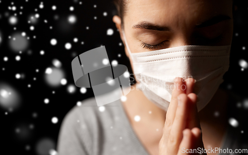 Image of sick young woman in protective face mask praying