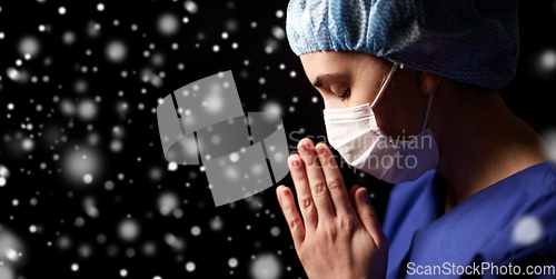 Image of female doctor or nurse in face mask praying