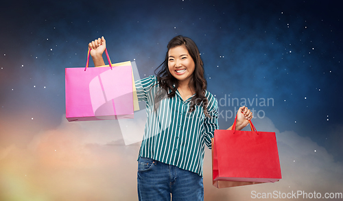 Image of happy asian woman with shopping bags on night sky