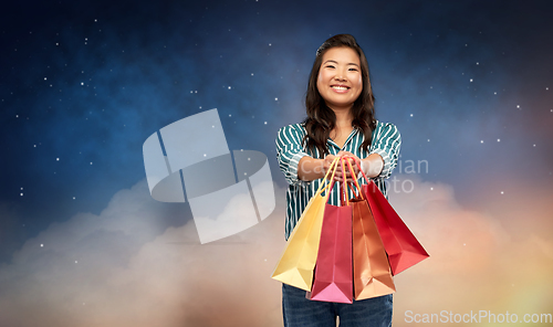 Image of happy asian woman with shopping bags on night sky