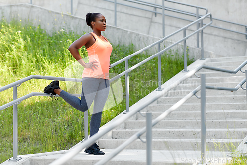 Image of young african american woman stretching outdoors