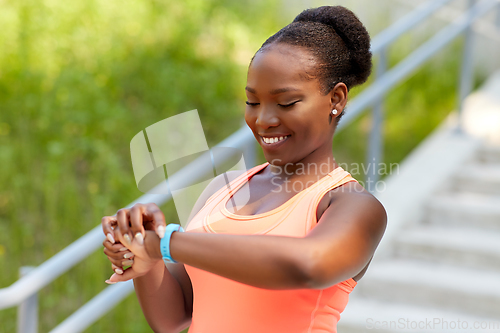 Image of happy african woman with fitness tracker outdoors