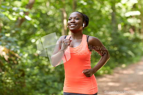 Image of happy african woman in earphones running in park