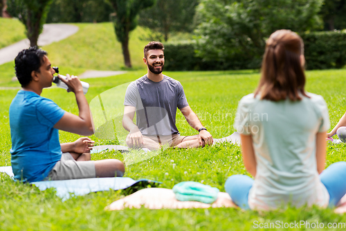 Image of group of people sitting on yoga mats at park