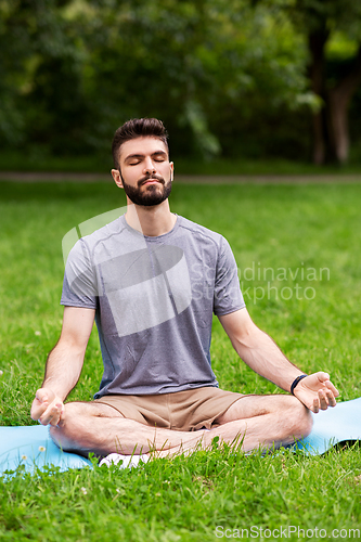 Image of young man meditating at summer park