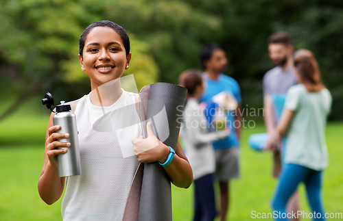 Image of smiling woman with yoga mat and bottle at park