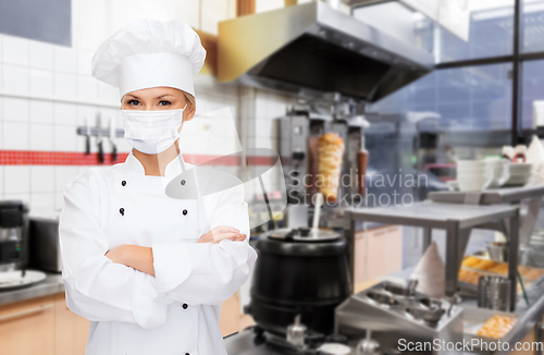 Image of female chef in mask with crossed arms at kitchen