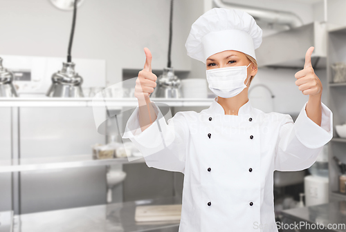 Image of female chef in mask showing thumbs up at kitchen