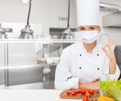 Image of female chef in mask showing ok sign at kitchen