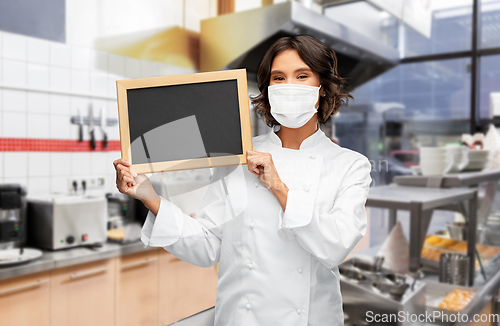 Image of female chef in mask with chalkboard at kitchen