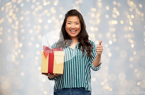 Image of happy asian woman with gift box showing thumbs up