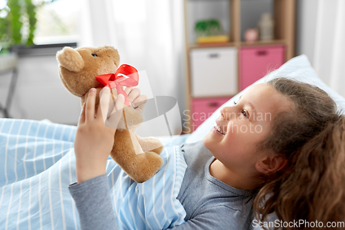 Image of happy little girl with teddy bear lying in bed