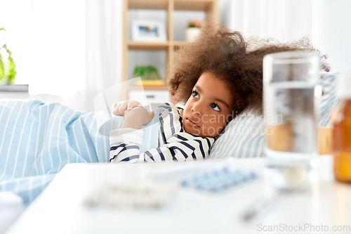 Image of sick african american girl lying in bed at home