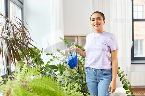 Image of african american woman watering plants at home