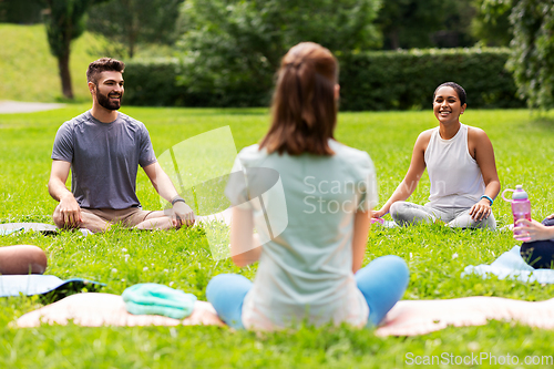 Image of group of people sitting on yoga mats at park