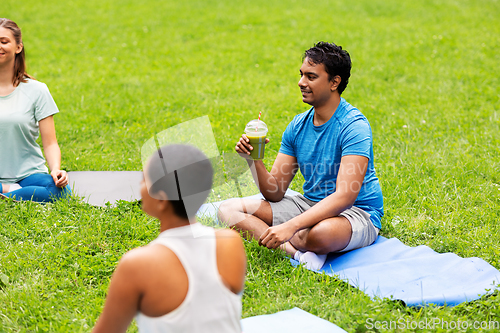 Image of group of people sitting on yoga mats at park