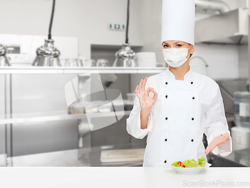 Image of female chef in mask showing ok sign at kitchen