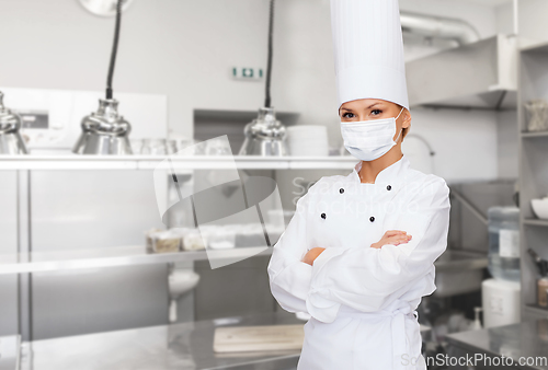 Image of female chef in mask with crossed arms at kitchen