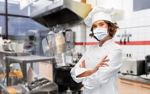 Image of female chef in mask with crossed arms at kitchen