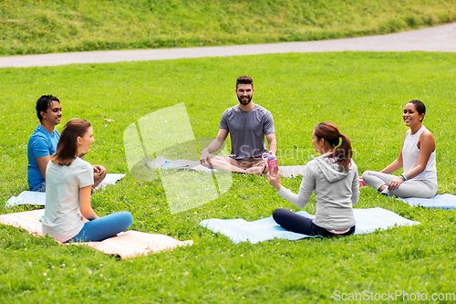 Image of group of people sitting on yoga mats at park