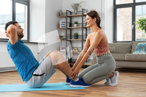 Image of man with personal trainer doing sit ups at home