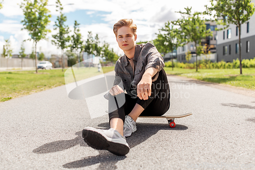 Image of teenage boy sitting on skateboard on city street