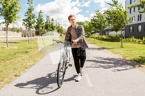 Image of young man with bicycle walking along city street