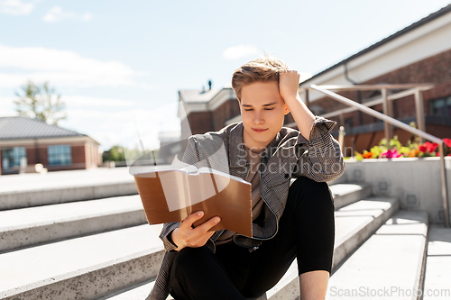 Image of young man or teenage boy reading book in city