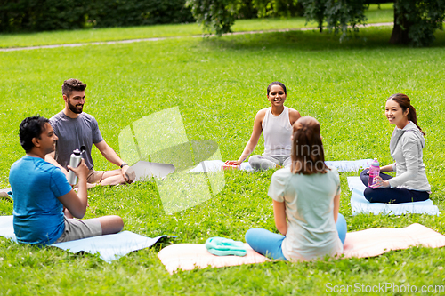 Image of group of people sitting on yoga mats at park