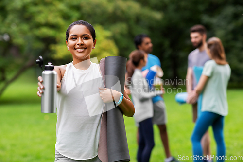 Image of smiling woman with yoga mat and bottle at park