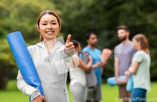 Image of smiling woman with yoga mat showing thumbs up