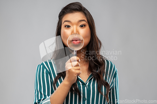 Image of happy asian woman with magnifying glass on lips