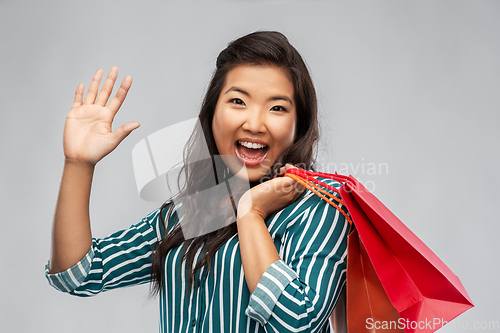 Image of happy asian woman with shopping bags waving hand