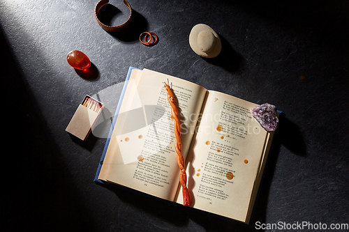 Image of magic book, wax candle, matches and gem stones