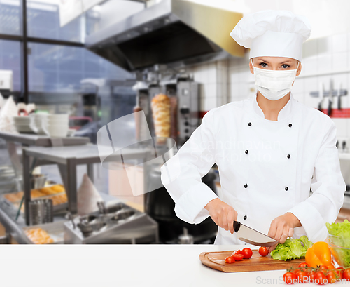 Image of female chef in mask cutting vegetables at kitchen