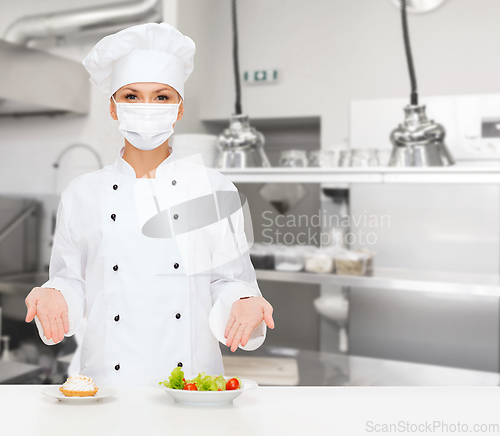 Image of female chef in mask showing food at kitchen