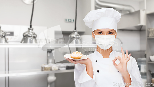 Image of female chef in mask showing ok sign at kitchen