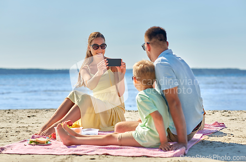 Image of family with smartphone photographing on beach