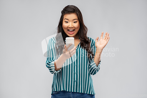 Image of happy asian woman with smartphone waving hand