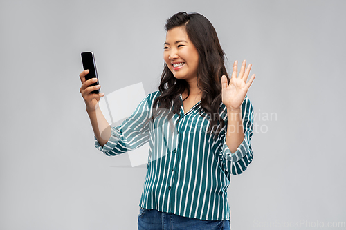 Image of happy asian woman with smartphone waving hand