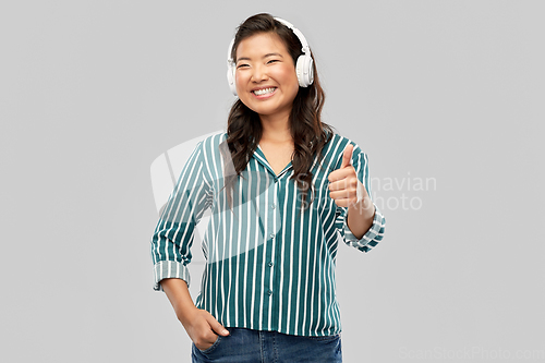 Image of happy asian woman in headphones showing thumbs up