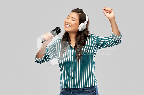 Image of asian woman in headphones with hairbrush singing