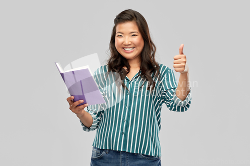 Image of happy asian woman with book showing thumbs up