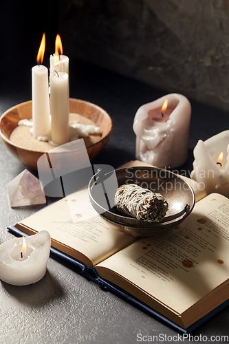 Image of magic book, sage, burning candles and ritual staff