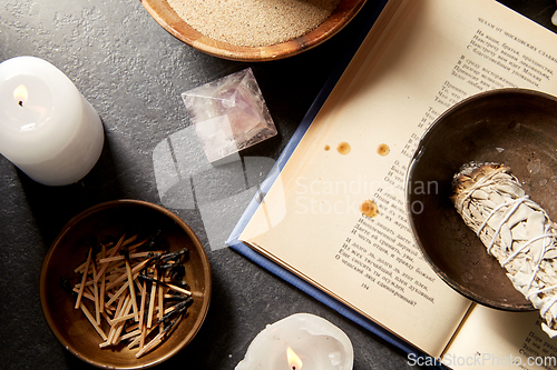 Image of magic book, sage, burning candles and ritual staff