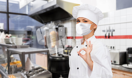 Image of female chef in mask showing ok sign at kitchen