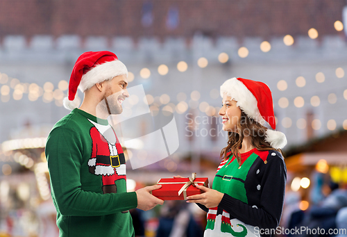 Image of happy couple in christmas sweaters with gift box