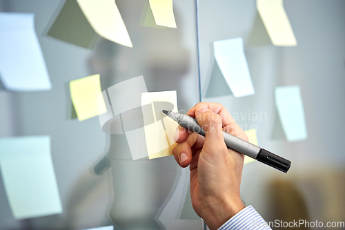 Image of hand with marker and sticker on glass at office